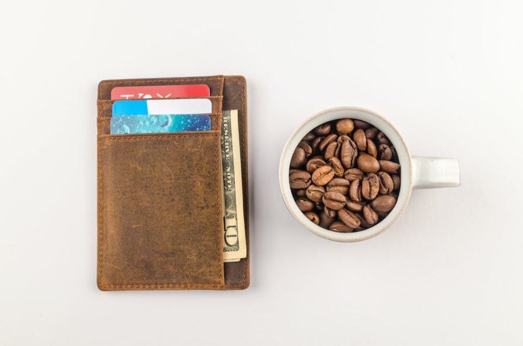 wallet with credit cards and cash in it beside a coffee cup full of coffee beans