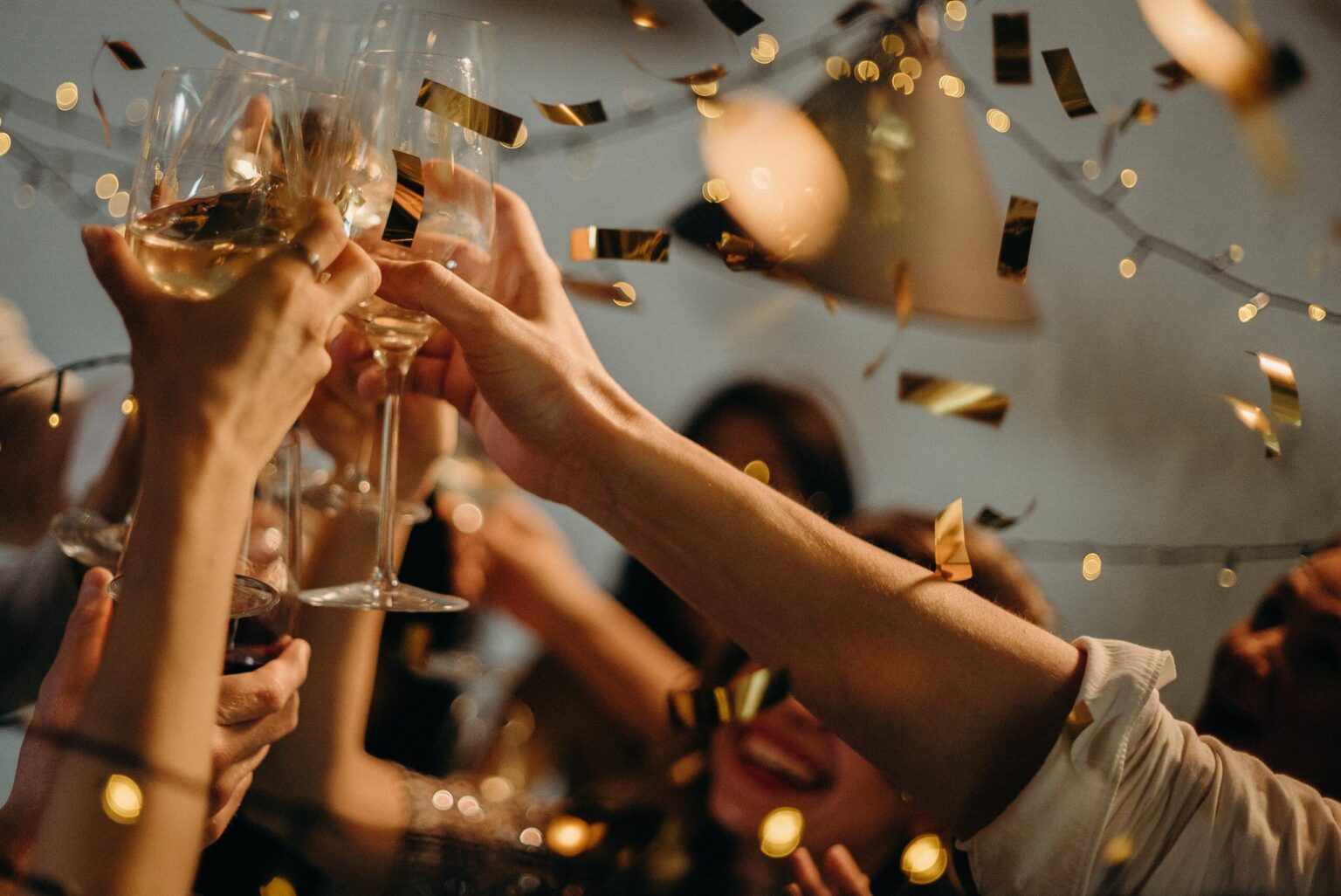 people holding champagne up in the air to toast with golden confetti falling around