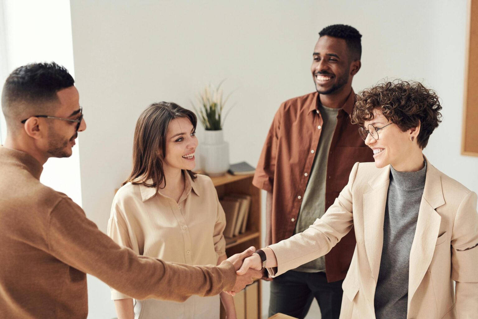 four people in a neutrally colored room with two shaking hands in the front