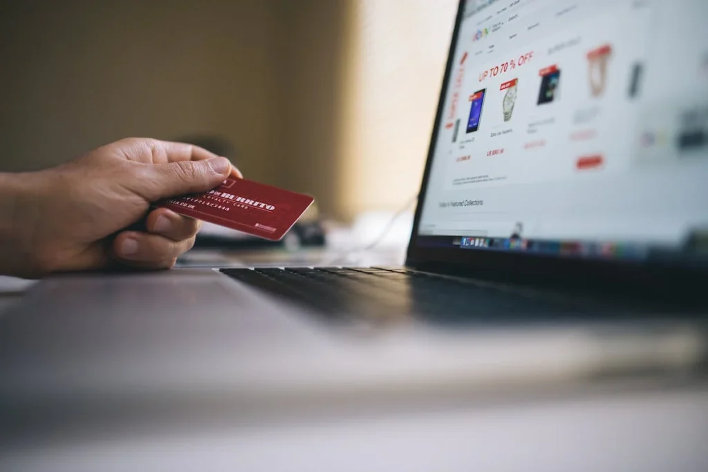 hand holding credit card beside a laptop open to an Temu comparison to Amazon