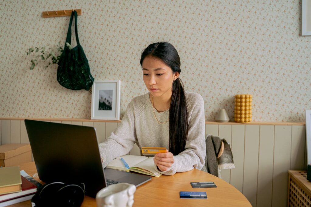 Woman holding credit card over an open notebook and looking at her open laptop, setting up credit card protections for her eCommerce business